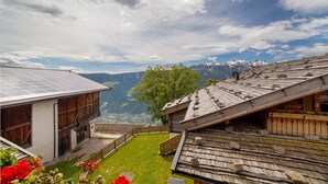 A traditional chalet with a sloped roof, a wooden deck, and a view of snow-capped mountains.