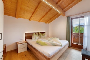 Un dormitorio con techo de madera, una cama con almohadas, una mesita de noche y una ventana con cortinas.