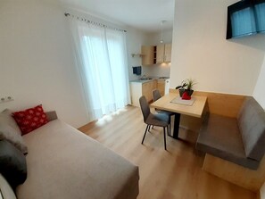 Ett modernt vardagsrum med en soffa, ett matbord med stolar, ett kök i bakgrunden och en tv som är monterad på väggen.