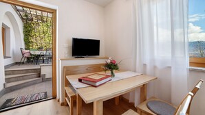 A room with a wooden table, a TV, a window with curtains, and a view of greenery outside. - Farmhouse 'Fröhlichhof Pergola' with Mountain View, Shared Pool and Wi-Fi (Algund)