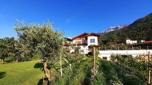 A two-story building with a balcony, surrounded by greenery and mountains in the background. - Farmhouse 'Fröhlichhof Pergola' with Mountain View, Shared Pool and Wi-Fi (Algund)