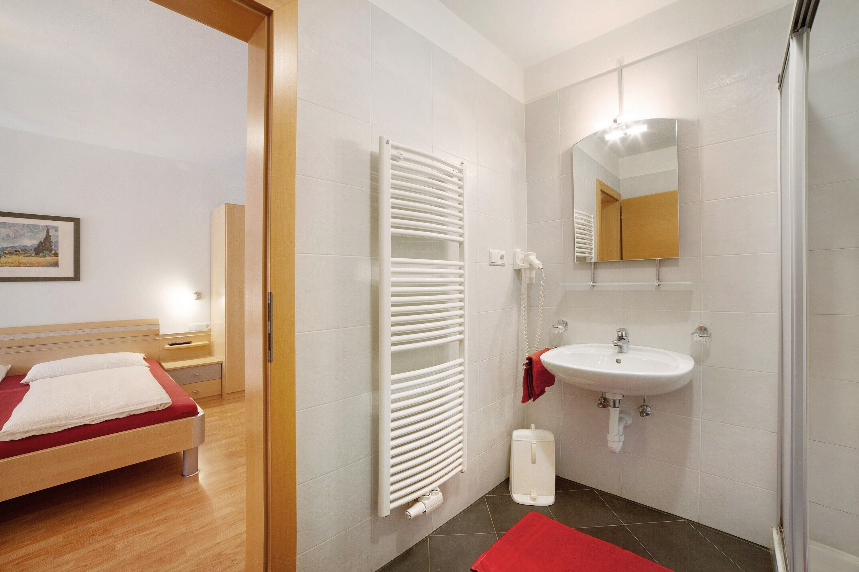 Quarto de hotel com uma cama, um radiador branco, uma pia e um espelho.