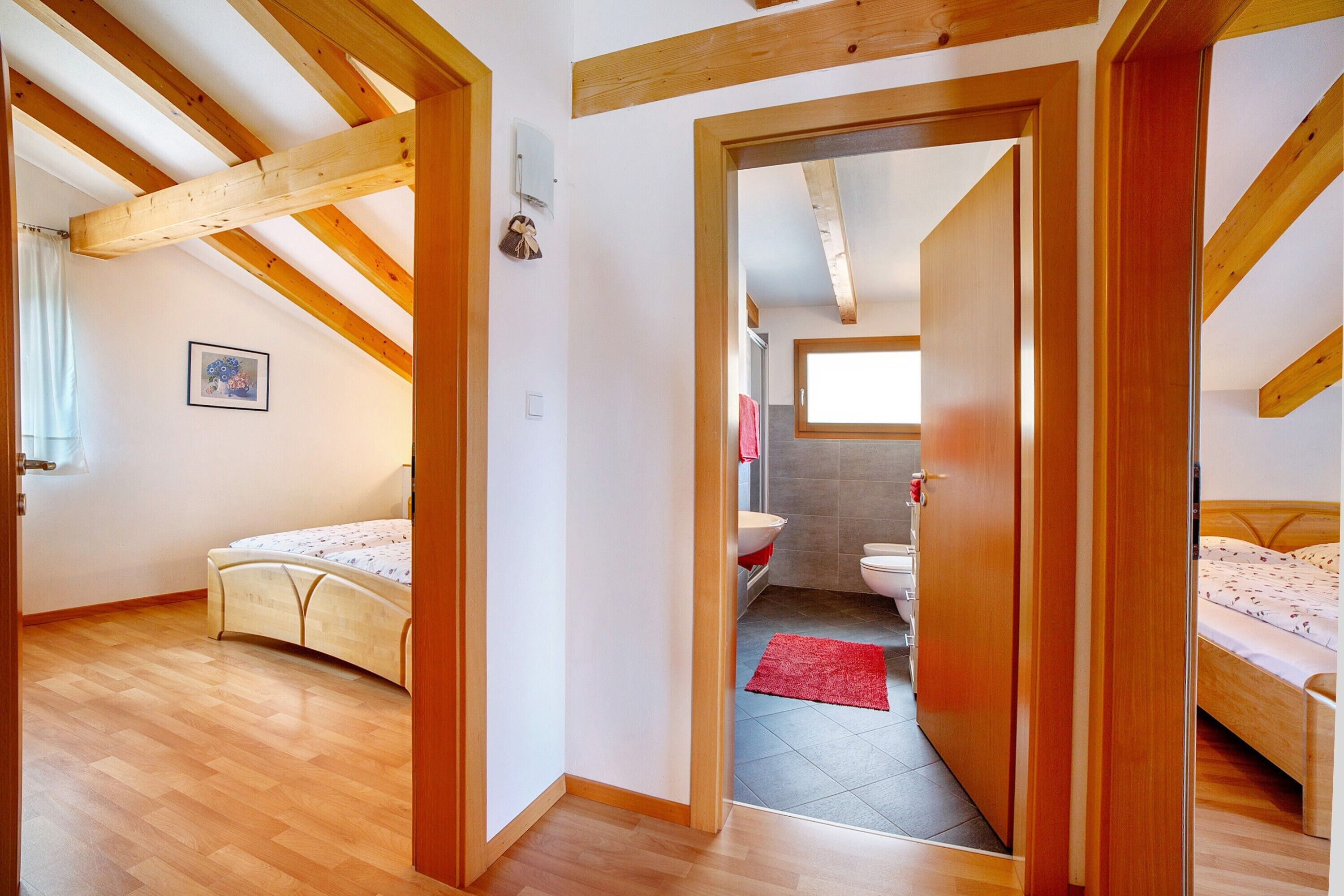 A bedroom with a wooden ceiling, a bed, and a red rug.
