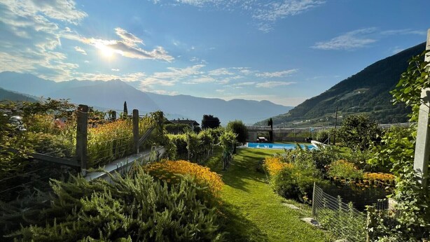 A garden with a pool, surrounded by mountains and a clear sky. - Farmhouse 'Fröhlichhof Wohnung Panorama' with Mountain View, Shared Pool and Wi-Fi (Algund)