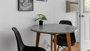 Un coin repas avec une table ronde en marbre, deux chaises noires, une plante en pot et deux tableaux encadrés au mur.
