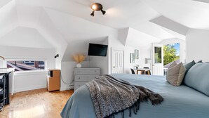 Une chambre moderne avec un grand lit, un téléviseur à écran plat, une commode et une fenêtre donnant sur un paysage urbain.