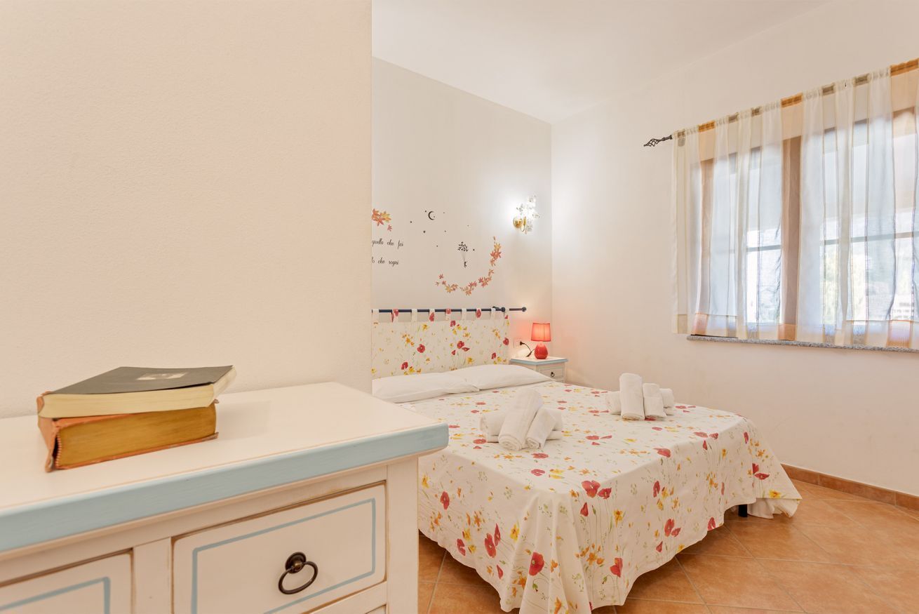 Une chambre avec deux lits, une table de chevet avec un livre, une petite table de nuit avec une lampe et une fenêtre avec des rideaux.