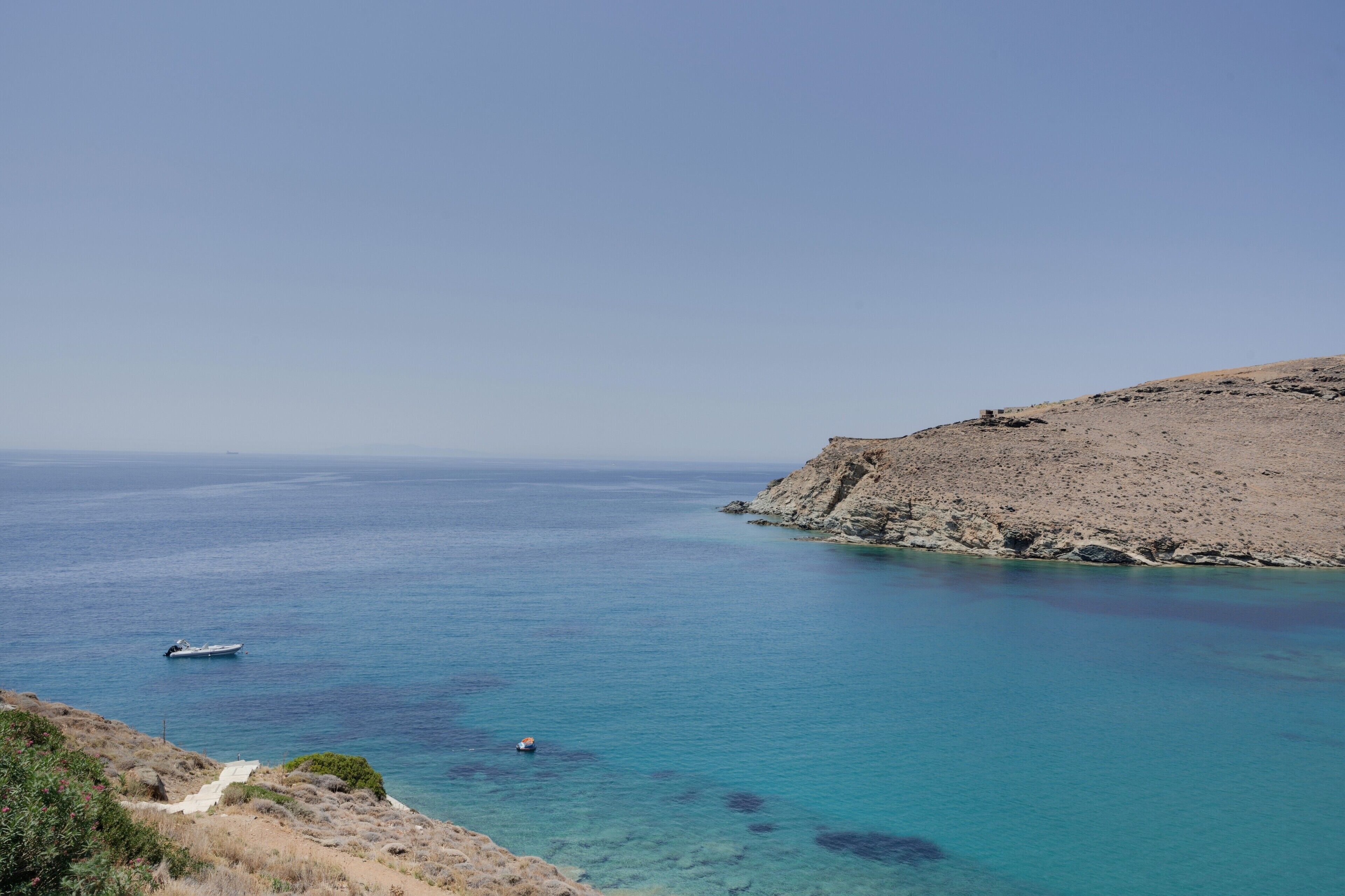 A coastal landscape with clear blue waters, rocky terrain, and a boat.