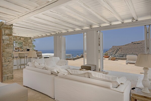 Un área de descanso moderna y luminosa, con pared de piedra, sofá blanco y vista al mar.