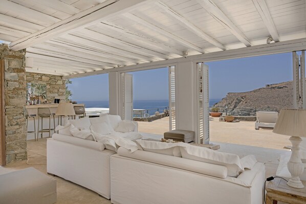 A white interior with a stone wall, a white sofa, and a view of the sea.