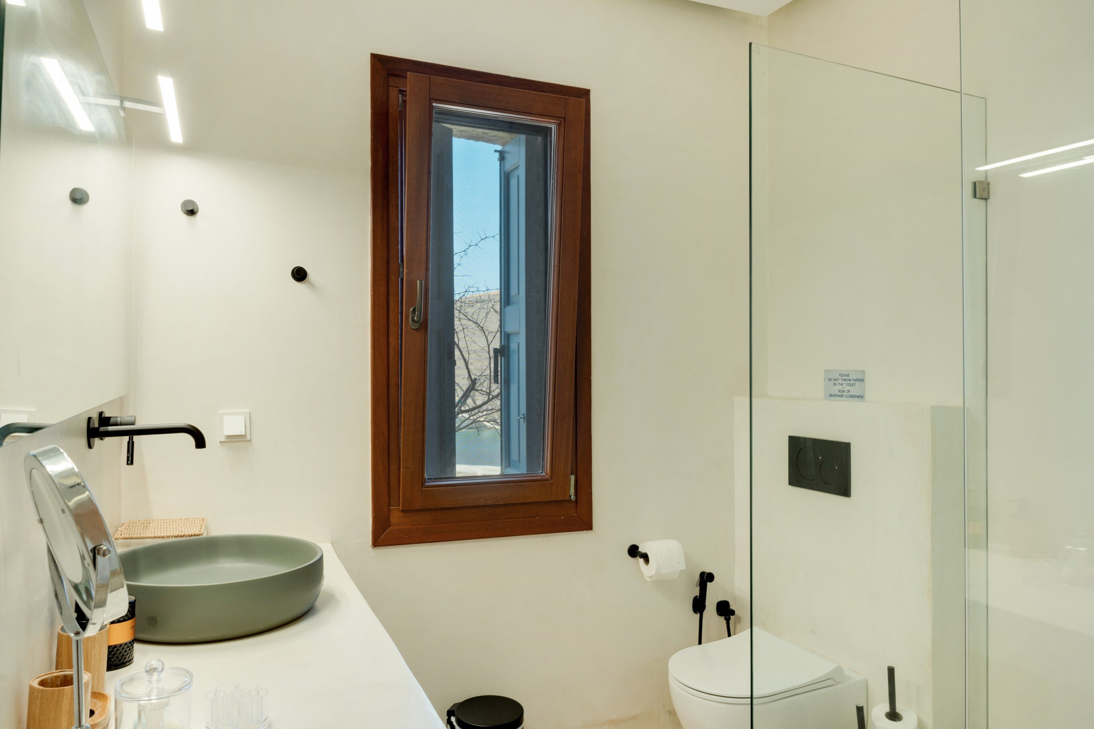 Une salle de bain moderne dotée d’une grande fenêtre, d’un lavabo avec un receveur, de toilettes et d’une douche à parois de verre.