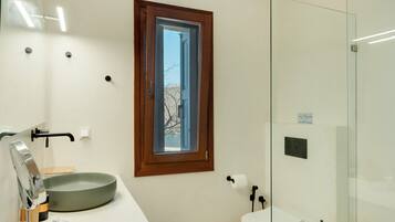 Une salle de bain moderne dotée d’une grande fenêtre, d’un lavabo avec un receveur, de toilettes et d’une douche à parois de verre.