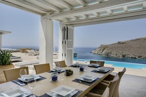 Comedor con una mesa dispuesta para cuatro, con vistas a una piscina y un acantilado.