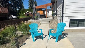 A patio area with two turquoise Adirondack chairs, a wooden pergola, and a white house in the background. - SHUSWAP GOLF AND LAKE ESCAPE
 (Blind Bay)