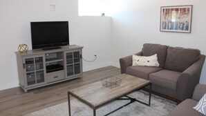 A living room with a flat-screen TV on a cabinet, a brown sofa, and a coffee table. - SHUSWAP GOLF AND LAKE ESCAPE
 (Blind Bay)