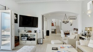 A modern living room with a television, white furniture, and a staircase leading to another room. - Studio Apartment "Blueros - Grey Suite" with Sea View, Private Pool & Wi-Fi (Syros)