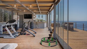A spacious room with a large window overlooking the sea, exercise equipment, and a wooden deck. - Studio Apartment "Blueros - Grey Suite" with Sea View, Private Pool & Wi-Fi (Syros)