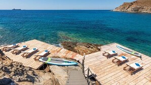 A wooden pier with lounge chairs and a surfboard, overlooking a clear blue sea and rocky coastline. - Studio Apartment "Blueros - Grey Suite" with Sea View, Private Pool & Wi-Fi (Syros)