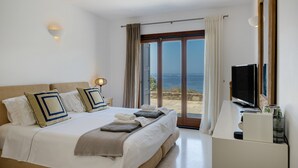 Ett hotellrum med en säng, ett skrivbord, en tv och utsikt över havet.