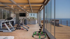 Ett modernt gym med träningsutrustning, en tv och utsikt över havet.