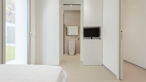 A modern hotel room with a bed, a TV, a bathroom with a toilet and sink, and a large window.