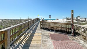 En træpromenade, der fører til en strand under en klar himmel.