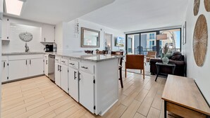 Et moderne køkken med hvide skabe, en central ø og et spiseområde med sofa og bord.