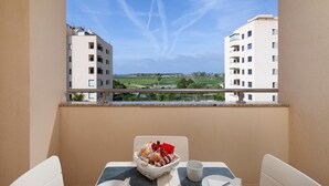 A balcony with a table set for two, a basket of snacks, and a clear view of buildings and greenery. - Playa Marinsa Beach – Pool, Padel, and Beach in Torre del Mar (Torre del Mar)
