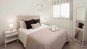 A neatly arranged bedroom with a bed, bedside tables, a wall decoration, a mirror, and a window with curtains. - Playa Marinsa Beach – Pool, Padel, and Beach in Torre del Mar (Torre del Mar)