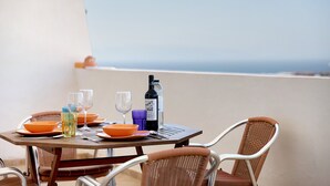 Une table dressée avec des assiettes orange, des verres et une bouteille de vin, sur un balcon offrant une vue panoramique.