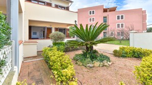 Un bâtiment à deux étages avec un jardin à l’avant, comprenant un palmier et divers arbustes.