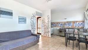 Un salon avec un canapé, un coin repas avec des chaises, une cuisine équipée d’une cuisinière et de placards, et des œuvres d’art murales.