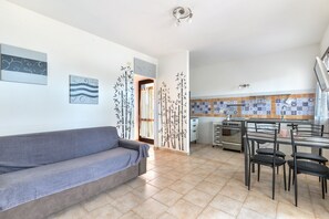 Una sala de estar con un sofá, un comedor con sillas, una cocina con estufa y alacenas, y decoración en la pared.