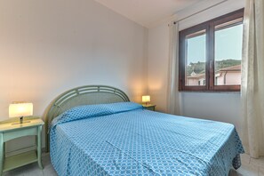 Une chambre à coucher avec un lit, deux lampes de chevet, une fenêtre avec des rideaux et une vue sur les bâtiments à l’extérieur.