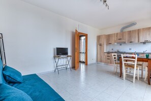 Un appartement moderne comprenant un espace de vie, une table à manger avec des chaises, une cuisine avec des meubles en bois et un téléviseur posé sur un meuble.