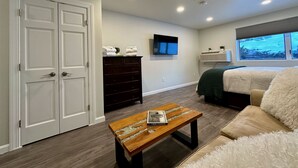 A bedroom with a bed, a TV mounted on the wall, a dresser, and a window with a view.