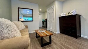 A living room with a beige sofa, a wooden coffee table, a dark wooden dresser, and a white door.