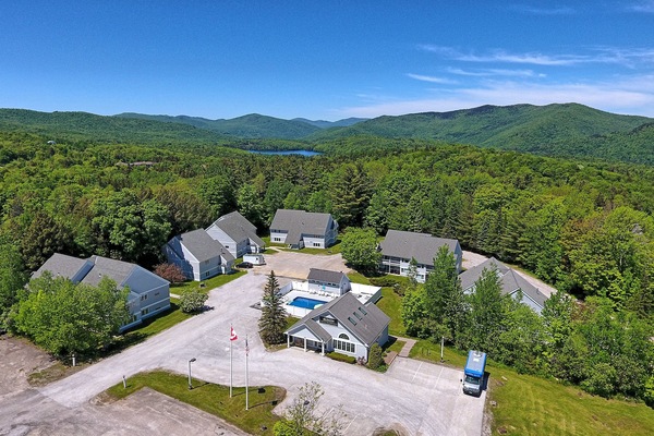 Buildings and access roads sit among dense woods, with mountain ridges and a small pond in the distance.