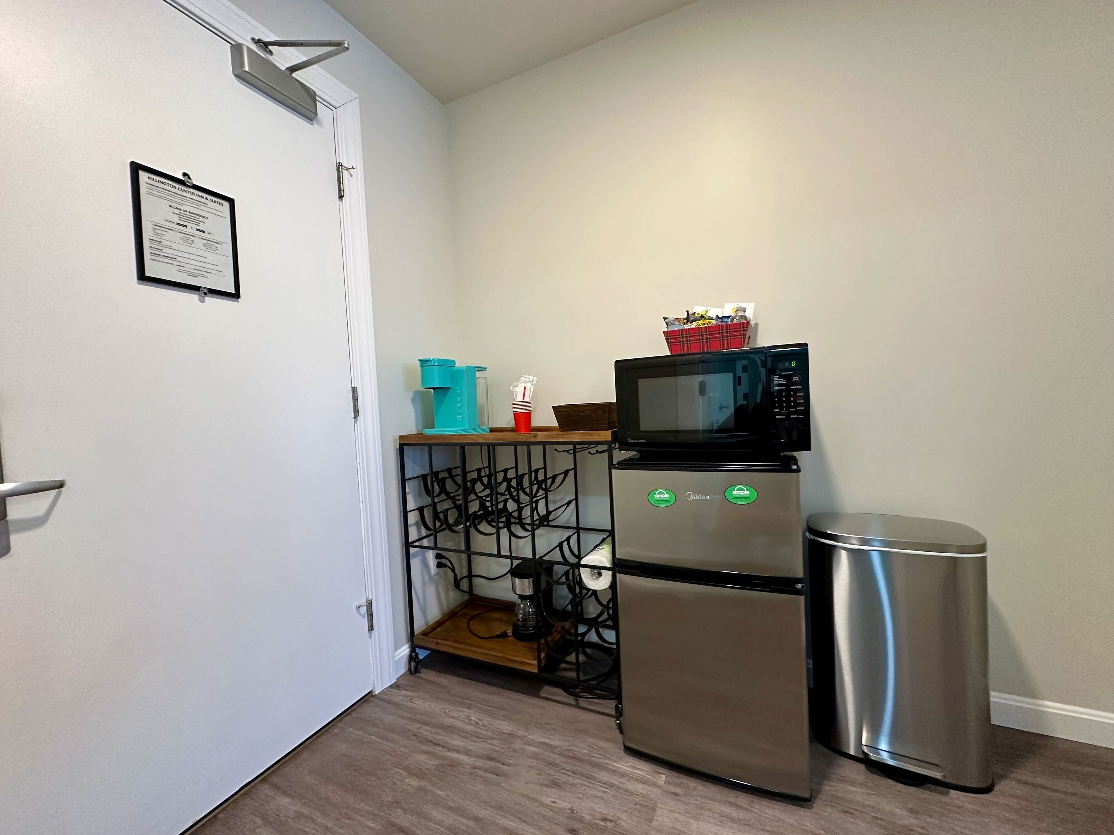 A compact kitchenette with a microwave, a small refrigerator, and a trash bin.