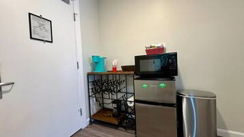 A compact kitchenette with a microwave, a small refrigerator, and a trash bin.