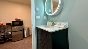 A modern bathroom with a round mirror, sink, and a trash bin.