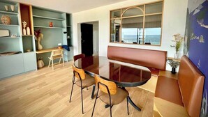 Un salon moderne avec une table à manger en verre, deux chaises en bois, un canapé, une bibliothèque et une grande fenêtre donnant sur un beau paysage.