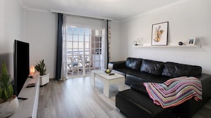 A modern living room with a black leather sofa, a white coffee table, a flat-screen TV, and a potted plant. - Vacation Apartment 'Las Teresitas Beach' with Mountain View, Balcony and Wi-Fi (San Andres)