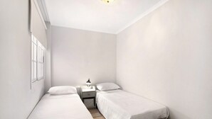 A small, clean room with two single beds, a nightstand, a lamp, and a woven bag. - Vacation Apartment 'Las Teresitas Beach' with Mountain View, Balcony and Wi-Fi (San Andres)