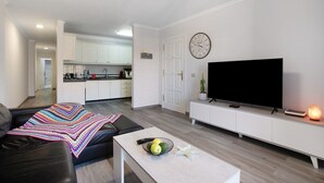 A modern living room with a sofa, a coffee table, a TV, and a kitchen in the background. - Vacation Apartment 'Las Teresitas Beach' with Mountain View, Balcony and Wi-Fi (San Andres)
