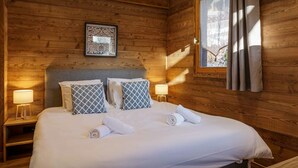 Un dormitorio con paneles de madera, una cama, dos lámparas de noche y un ventanal con cortinas.