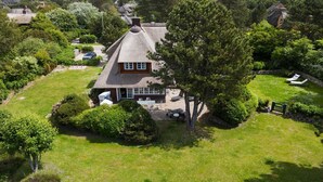 Une maison au toit de chaume, entourée d’une pelouse bien entretenue et d’arbres.