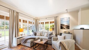 Un salon chaleureux avec un canapé d’angle, une table basse et une vue sur le jardin grâce à de grandes fenêtres.