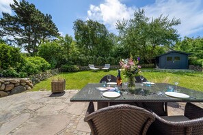An outdoor patio with a table set for dining, surrounded by stone walls and lush greenery.