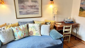 Una sala de estar acogedora con un sofá azul, cojines coloridos, un cuadro enmarcado y un escritorio de madera con libros.